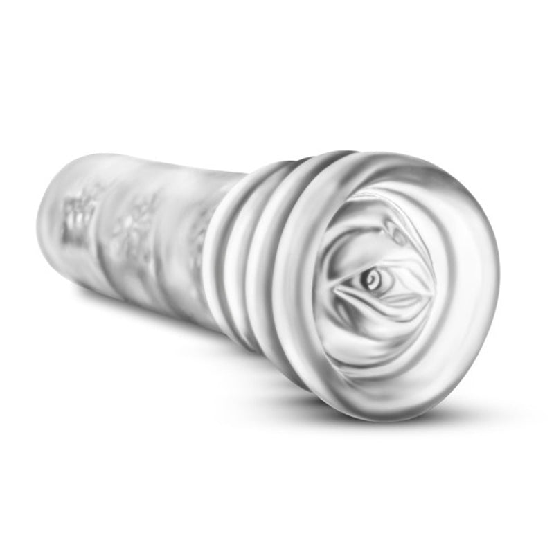 The All Nighter Glow in the Dark Textured Clear Self Lubricating Stroker by Blush is a clear, cylindrical, ultra-stretchy sleeve with inner ridges designed for tactile stimulation. Semi-transparent and resting on a white surface with a slight tilt, it reveals its inner structure as a discreet stroker.