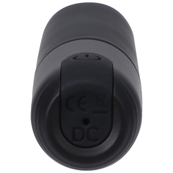 An up-close shot of the Beginner Classic Black Silicone Bullet Vibrator In a Bag by Doc Johnson, shaped like classic lipstick and USB rechargeable, viewed from the base. The base features a small round button labeled "DC" along with CE certification symbols and disposal instructions. The device boasts a smooth matte finish.