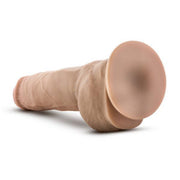 The Blush Big Boy 10 Inch Dual Density Suction Cup Dildo - Vanilla is shown horizontally, resting on a neutral background. This realistic silicone dildo features a veined shaft and a pronounced head to mimic the appearance of human anatomy. Its flesh-colored design highlights its textured details, while the strong suction cup base ensures stability during use.
