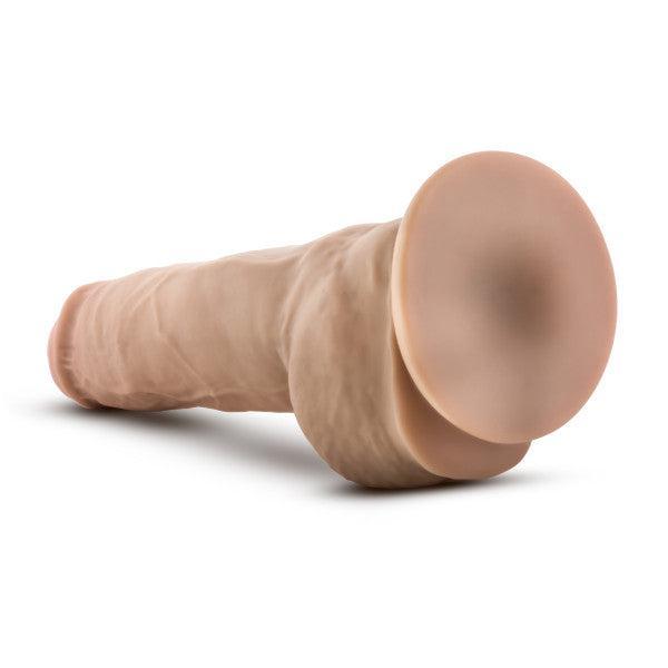 The Blush Big Boy 10 Inch Dual Density Suction Cup Dildo - Vanilla is shown horizontally, resting on a neutral background. This realistic silicone dildo features a veined shaft and a pronounced head to mimic the appearance of human anatomy. Its flesh-colored design highlights its textured details, while the strong suction cup base ensures stability during use.