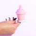 A hand with long, painted nails holds the Cake Eater Clitoral Stimulator Tongue Vibrator in pink, shaped like a cupcake with a soft swirl top, against a white background.