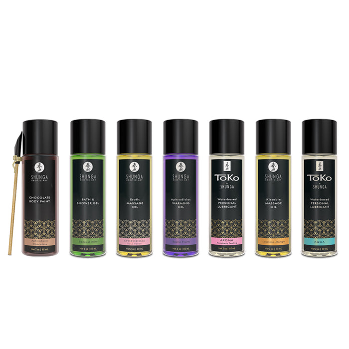 Seven bottles from the Shunga Advent Calendar of Desires—featuring body paint, bath gel, massage oils, aphrodisiac oils, and personal lubricant—are lined up side by side with a small brush beside the first; a sensual gift set for 25 days of pleasure.