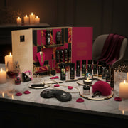 The Shunga Advent Calendar of Desires – 25 Days of Luxury, Pleasure & Passion is displayed on a marble table with candles, rose petals, wine, an eye mask, and a feather tickler for a sensual gift set experience.