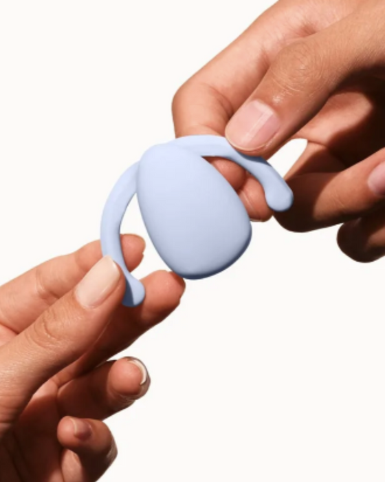 Dame Eva Hands-Free Silicone Clitoral Vibrator - Ice Blue being held by two hands on a white background