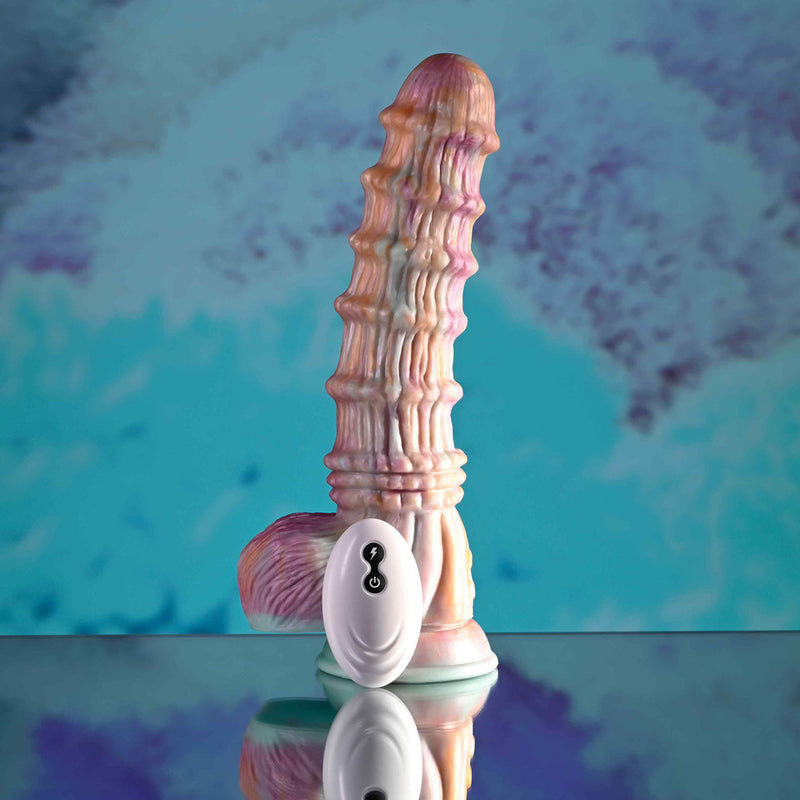 The Fantasy Ultra Textured Vibrating Remote Control Creature Dildo, with a pastel, ribbed form, stands upright on a reflective surface. Its small oval remote with two buttons lies in front, set against a blue-purple abstract background.
