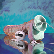 The Fantasy Ultra Textured Vibrating Remote Control Creature Dildo, with a textured silicone design, charging cable, USB plug, and oval remote (open battery compartment), is displayed on a reflective surface against an aqua-purple background.