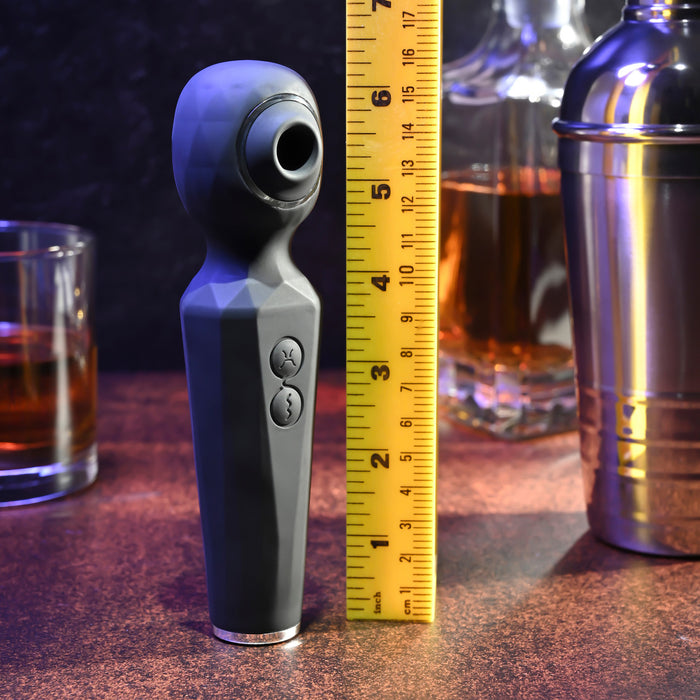 The Rainbow Sucker Wand + Clitoral Suction Vibrator, featuring a black geometric texture and standing about 6 inches tall beside a yellow measuring tape, is pictured on a bar surface with a whiskey glass and cocktail shaker in the background.