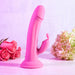 The Somebunny to Love Uncut Look Rabbit Vibrator, in pink with a suction base and clitoral stimulator, stands upright on a light surface among pink roses and hydrangeas against a pale backdrop.