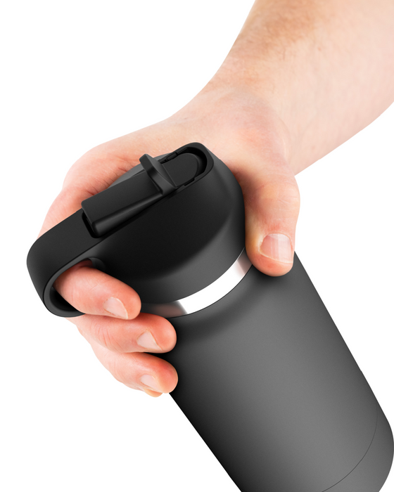 A hand is holding a black travel mug with a snap-on lid and a carrying handle, reminiscent of the discreet design of the Fuck Flask Pussy Stroker Disguised as a Water Bottle - Vanilla by Pipedream Products. The mug has a sleek, matte finish and a silver band around the top. The background is plain white.