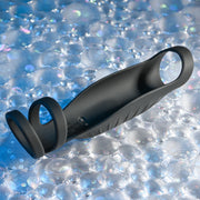 The Rocketeer Vibrating Penis Enhancer Sheath, a black body-safe silicone sheath with three loops, rests on a textured, iridescent bubble-patterned surface.