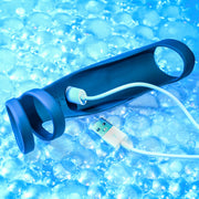 The Rocketeer Vibrating Penis Enhancer Sheath, made of blue body-safe silicone with a USB charging cable, is displayed on a shiny, bubble-textured blue surface.