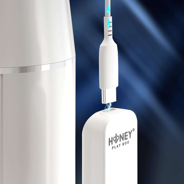 Close-up of the Blanche Thrusting Auto Blowjob Masturbator by Honey Play Box being connected to a USB-C cable, with blue arrows showing the direction, set against a dark, blurred background.