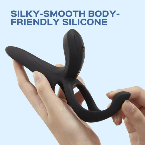 A hand holds the Pleasure Pivot Vibrating Cock Ring with Clit Stimulator, made of black body-friendly silicone, against a light blue background. Dark blue text above says, "Silky-Smooth Body-Friendly Silicone.