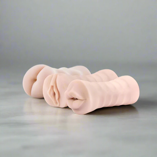 The M for Men 3-Pack Self-Lubricating Vibrating Masturbation Sleeve Kit - Vanilla displays three realistic, detailed silicone sleeves on a gray surface, each designed to provide a lifelike experience for adult pleasure.