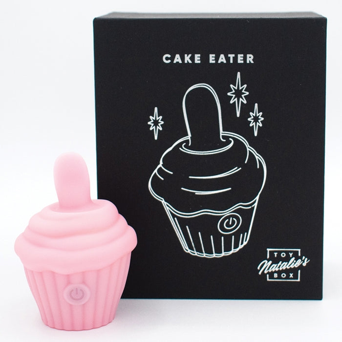 The Cake Eater Clitoral Stimulator Tongue Vibrator in pink, shaped like a cupcake, is displayed next to a black box with a white cupcake illustration and the words "Cake Eater" and "Toy Natalie's Box.