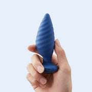 A hand holds the Noah App-Enabled Rotating Butt Plug, featuring a blue ridged design and control buttons on the base, against a light blue background.
