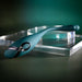 The Pinpoint Perfection Flexible Slim Vibrator, featuring a sleek teal design with a black accent, is displayed on a clear acrylic platform against a dark green gradient background.