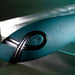 A close-up of the Pinpoint Perfection Flexible Slim Vibrator in sleek teal, featuring a black power button and Playboy bunny logo, set against a glass and metal background with dramatic lighting.