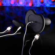 The Playboy Sittin' & Spinnin' Hands Free G-Spot Vibrating Grinder Pad and a black silicone rotating penetrator, both with white USB charging cables, rest on a glossy black surface with a colorful abstract pattern in the background.
