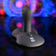 The Playboy Sittin' & Spinnin' Hands Free G-Spot Vibrating Grinder Pad, featuring a ribbed shaft and three buttons, sits on a reflective surface against swirling blue, pink, and purple lights—modern pleasure redefined.