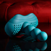 The Playboy Have a Seat Remote Control Grinding Vibrator Pad, made from body-safe silicone with a curved, ridged design and suction cup base, sits on a reflective black surface in front of a plush red cushion.