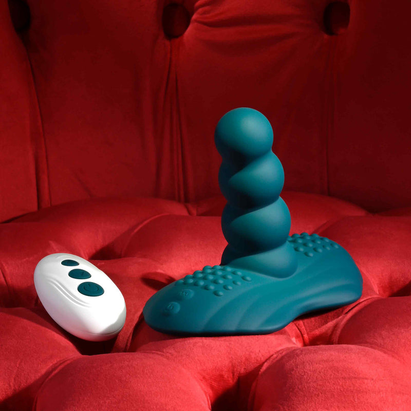 The Playboy Have a Seat Remote Control Grinding Vibrator Pad, in teal body-safe silicone with a textured surface and suction cup base, rests on a tufted red velvet background.