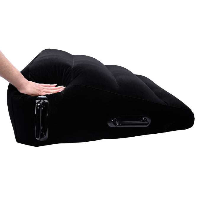 A person lightly pressing on the Pivot Plus Large Inflatable Sex Positioner Wedge Cushion from Sportsheets, demonstrating its flexibility and softness. The black wedge pillow is designed for ergonomic support and features handles on the sides for easy adjustment and positioning.