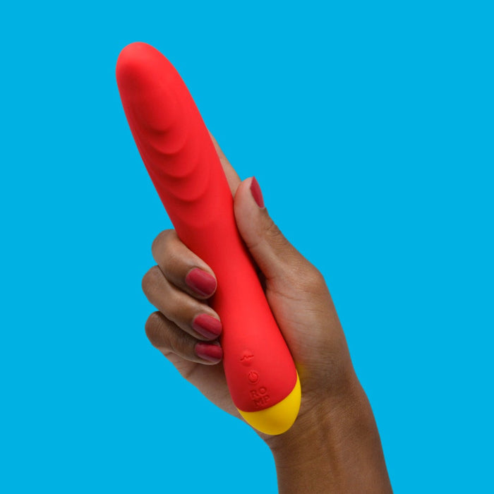 A hand with painted nails holds the Romp Hype Rechargeable Silicone G-Spot Vibrator against a bright blue background.