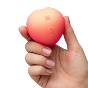 Hand holding a compact, soft silicone Romp Peach Pleasure Air Stimulator with a pink to peach gradient.