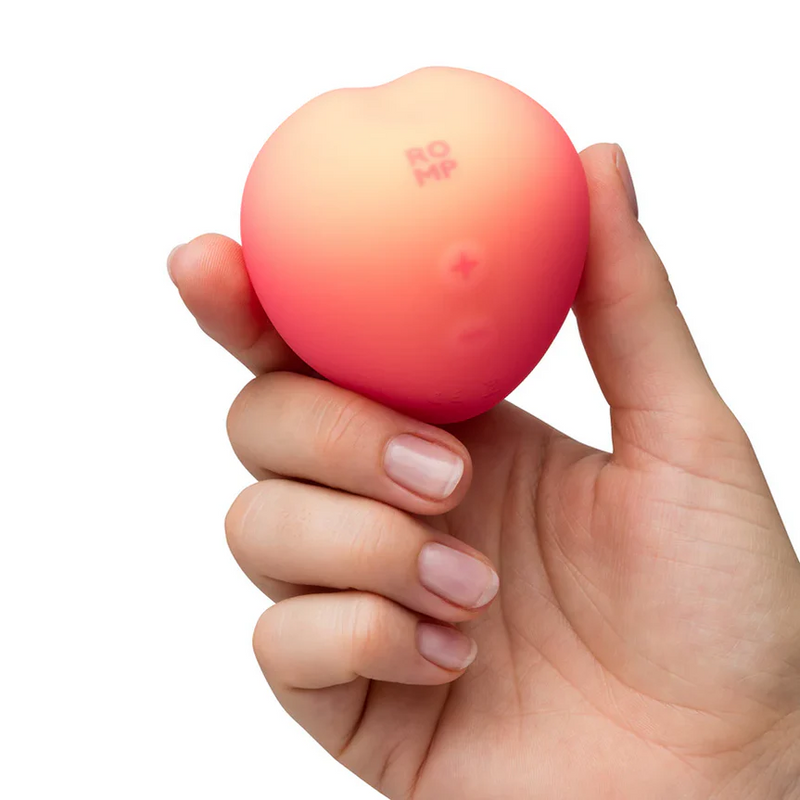 Hand holding a compact, soft silicone Romp Peach Pleasure Air Stimulator with a pink to peach gradient.