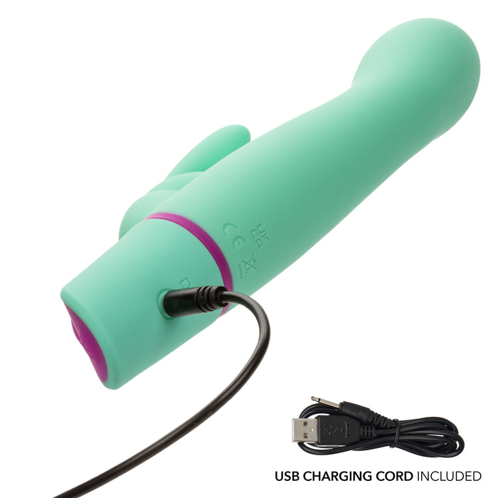 The Love Bunny Rockin’ G Triple Motor Rabbit Vibrator in turquoise is shown with its USB charging cord plugged in; the coiled cord rests nearby on a white background. Text reads: "USB CHARGING CORD INCLUDED.