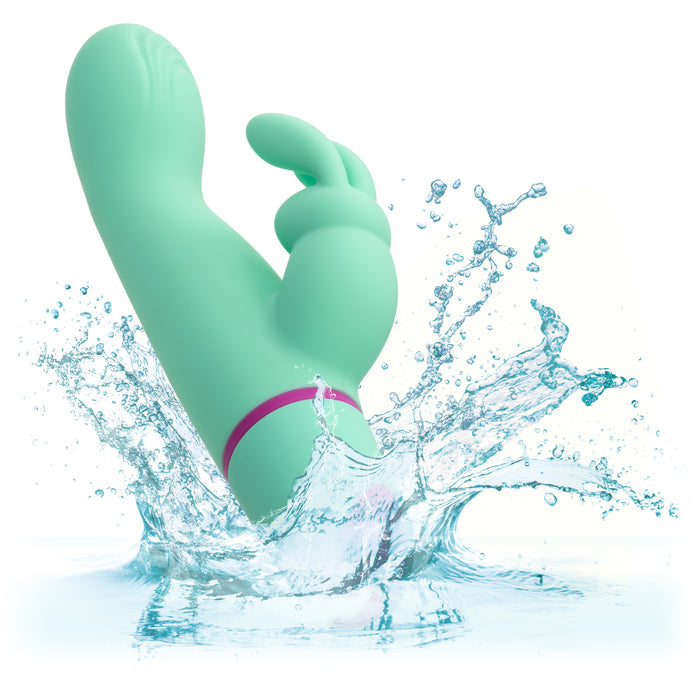 The mint green Love Bunny Rockin’ G Triple Motor Rabbit Vibrator, featuring a curved tip and smaller extension, splashes into clear water, showcasing its waterproof design and suitability for wet environments.