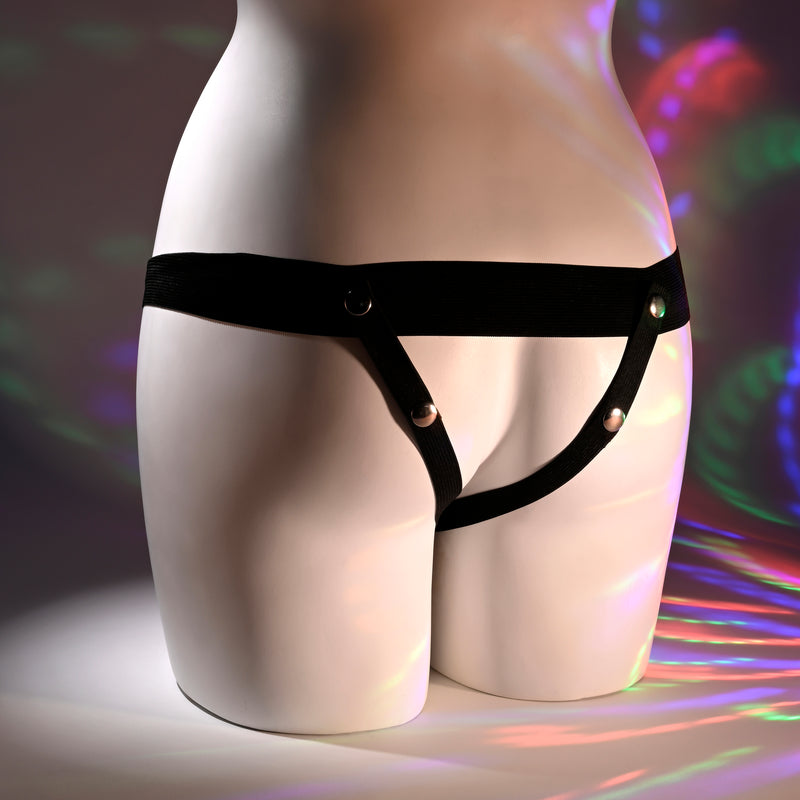 A mannequin torso is shown from behind, wearing the Our First Hollow Strap-On Dildo + Harness Set - Vanilla. Colorful circular light patterns are projected onto the background and lower half of the mannequin.