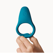 A hand holds up the Dame Hug Adjustable Vibrating Cock Ring for Couples, featuring a blue silicone design with a wider, flat top, against a plain white background.
