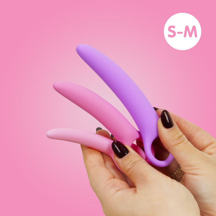 A hand with dark nail polish holds the Skins Care Curved Vaginal Dilators 3-Piece Set (Small / Medium), featuring pastel medical-grade silicone dilators in varying sizes, against a pink background with an "S-M" white circle.