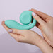 A person with neatly manicured nails holds the Snail Gizi Compact Ultra Powerful 2 Motor Dual Stimulating Vibrator - Blue from Snail Vibe, a light turquoise-colored silicone sex toy designed with a spiral pattern at one end and a curved, smooth end at the other, against a plain background.