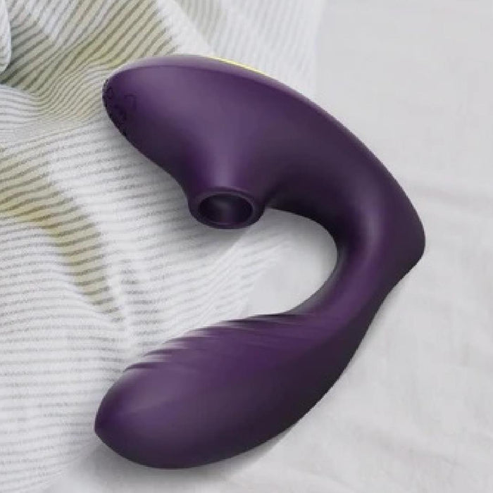 The Tracy's Dog OG Clitoral Sucking G-Spot Vibrator, in purple silicone with a curved design, rests on a white and gray striped fabric surface.
