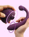 Hands holding and demonstrating the design and functionality of a modern, purple Tracy's Dog OG 3 Clitoral Suction & G-Spot 2 in 1 Vibrator with intuitive controls.