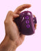 A hand squeezing a purple Tracy's Dog OG 3 Clitoral Suction & G-Spot 2 in 1 Vibrator with a gel-like liquid oozing out from the mesh.