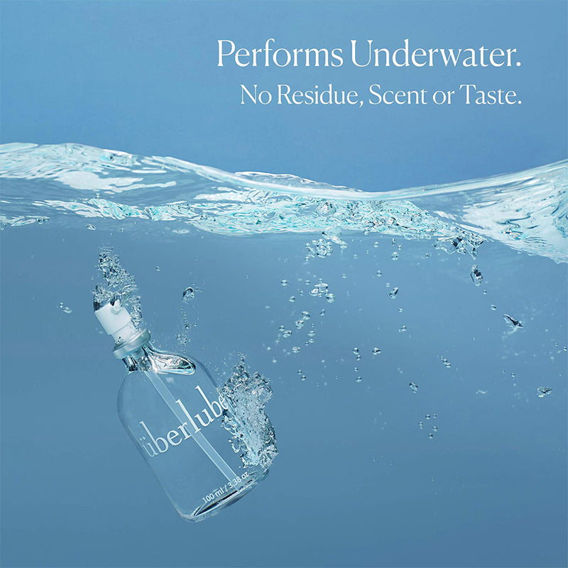 A clear bottle labeled "UberLube Premium Silicone Lubricant 50 ml" is underwater with bubbles. Text above: "Performs Underwater. No Residue, Scent or Taste." Features a long-lasting lube formula, set against blue water shades.