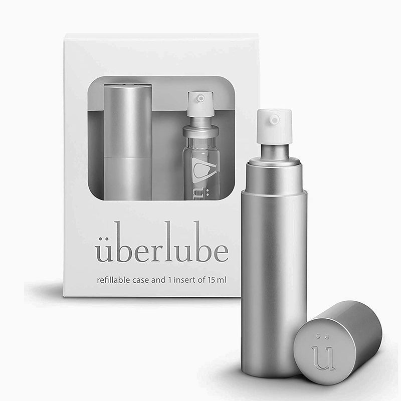 The UberLube Premium Silicone Lubricant Travel Spray 15 ml (Silver) is shown with a matching cap before a white box featuring a clear window that reveals another identical bottle inside. The box confirms it contains the 15 ml size.