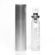 A clear glass bottle labeled "UberLube Premium Silicone Lubricant Travel Spray 15 ml (Silver)" stands beside a sleek silver cylindrical case, both set against a white background.