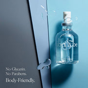 A clear glass spray bottle labeled "UberLube Premium Silicone Lubricant 50 ml" sits on a blue surface with water droplets. Text: No Glycerin. No Parabens. Body-friendly silicone lube for long-lasting use and anti-chafe protection.