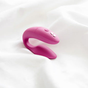 A dusty pink We-Vibe Sync 2 wearable couples vibrator with remote and app controls rests on a soft white fabric background.