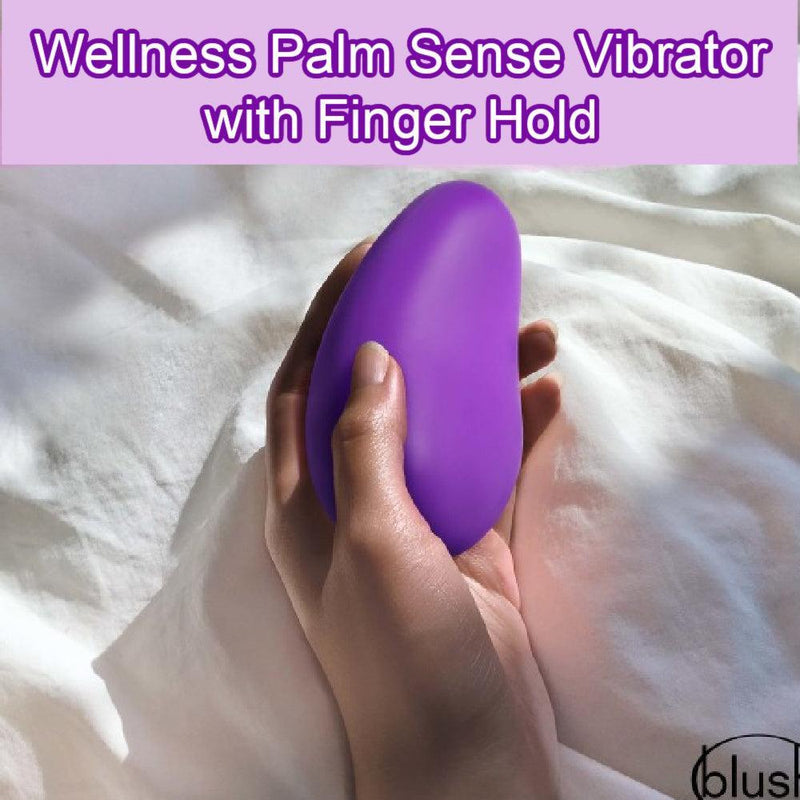 A hand holding a purple, teardrop-shaped silicone vibrator with "Wellness Palm Sense Rumbly External Vibrator with Finger Hold" written at the top in purple text. The background features a soft, white fabric. The brand name "Blush" is visible in the lower right corner.