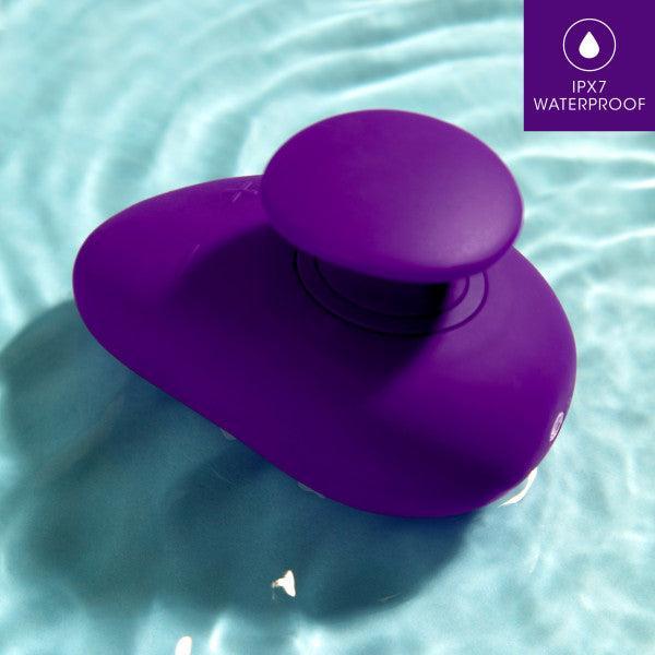 A purple Wellness Palm Sense Rumbly External Vibrator with Finger Hold by Blush rests on a rippling water surface. The top-right corner features a label stating "IPX7 Waterproof." This waterproof, rechargeable massager, made of premium silicone, promises both durability and comfort with its ergonomic design.