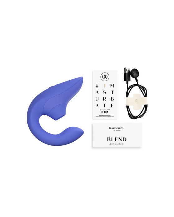 A blue, ergonomically shaped adult toy with a curved handle, designed for dual stimulation and G-spot vibrations, is placed next to a white manual, a quick start guide labeled "Womanizer Blend Pleasure Air Clitoral & G-Spot Rabbit - Blue," and a black USB charging cable with adapter.