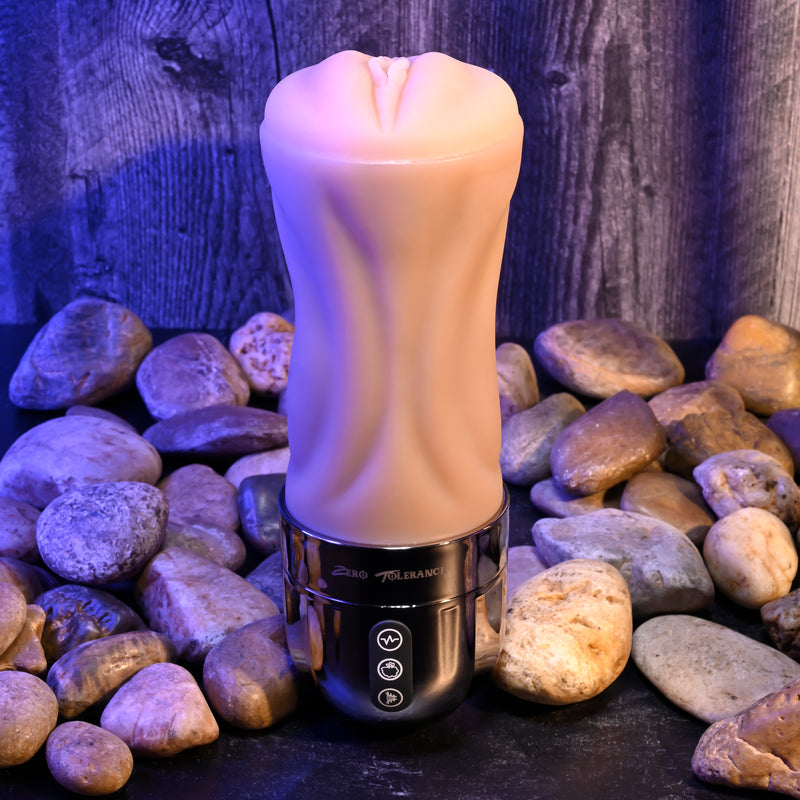 The Tight Lipped Vibrating Vanilla Stroker with Suction stands upright on a dark surface among river stones, its textured body and black base highlighted by purple-blue light against a wooden backdrop. Includes a free movie download.