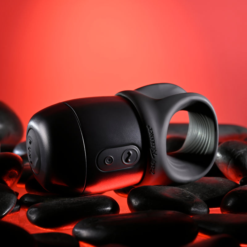 The Wet It Be Hand Held Vibrating Masturbator with Lube Dispenser, in sleek black silicone with control buttons, is displayed on smooth black stones against a bold red background.