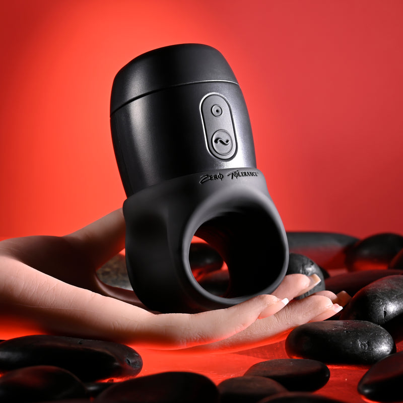 A hand holds the Wet It Be Hand Held Vibrating Masturbator with Lube Dispenser, featuring front buttons, surrounded by dark smooth stones against a red background.